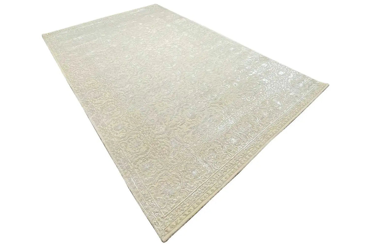Corner view of a light beige rug with a delicate pattern and textured surface.