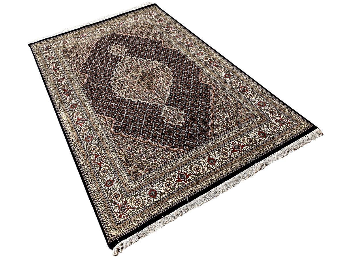 Tabriz-style rug viewed at an angle with an ornamental border and fringes along the edge