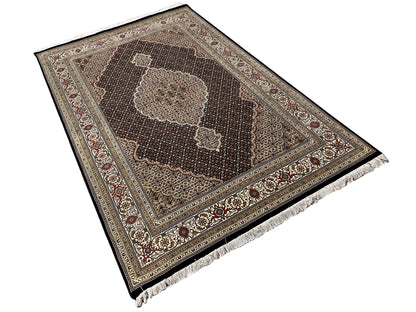 Tabriz-style rug viewed at an angle with an ornamental border and fringes along the edge