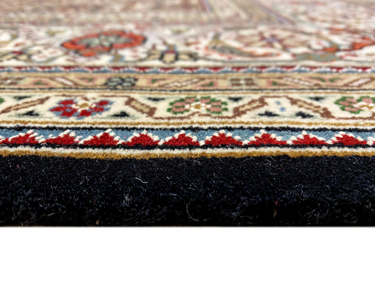 Side view of a Tabriz-style rug: border pattern at the top, dark pile and edge binding