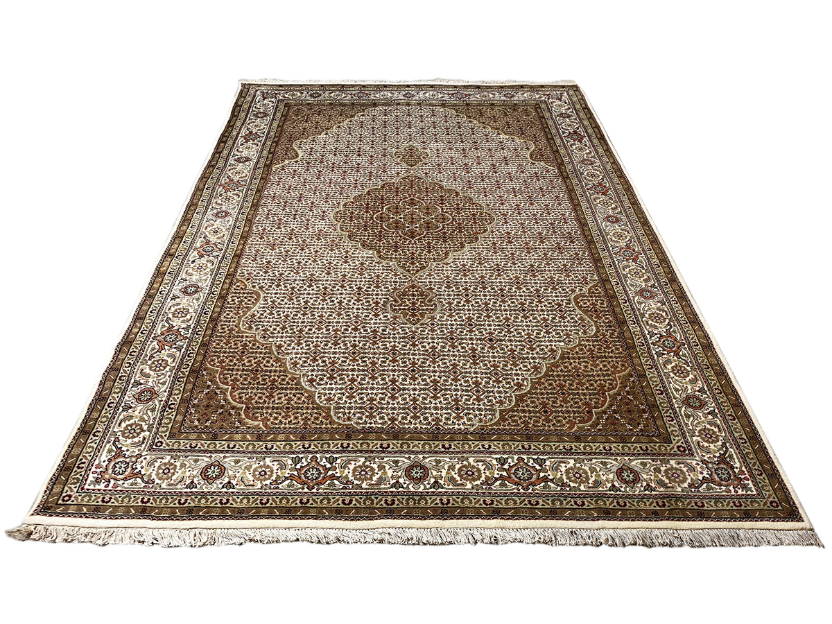 Rug: Corner view in beige/brown with an ornamental border and tassel fringe along the edge.