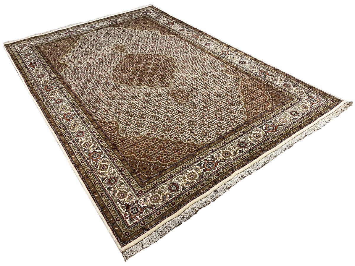Beige and brown rug spread out, photographed diagonally, with a decorative border and fringes.