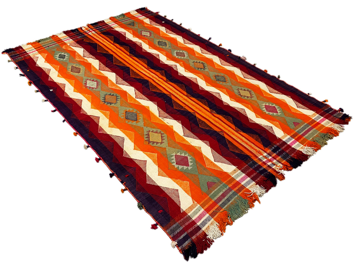 Jajim rug viewed diagonally from above, with zigzag and stripe patterns in orange and dark blue