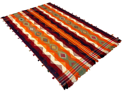Jajim rug viewed diagonally from above, with zigzag and stripe patterns in orange and dark blue