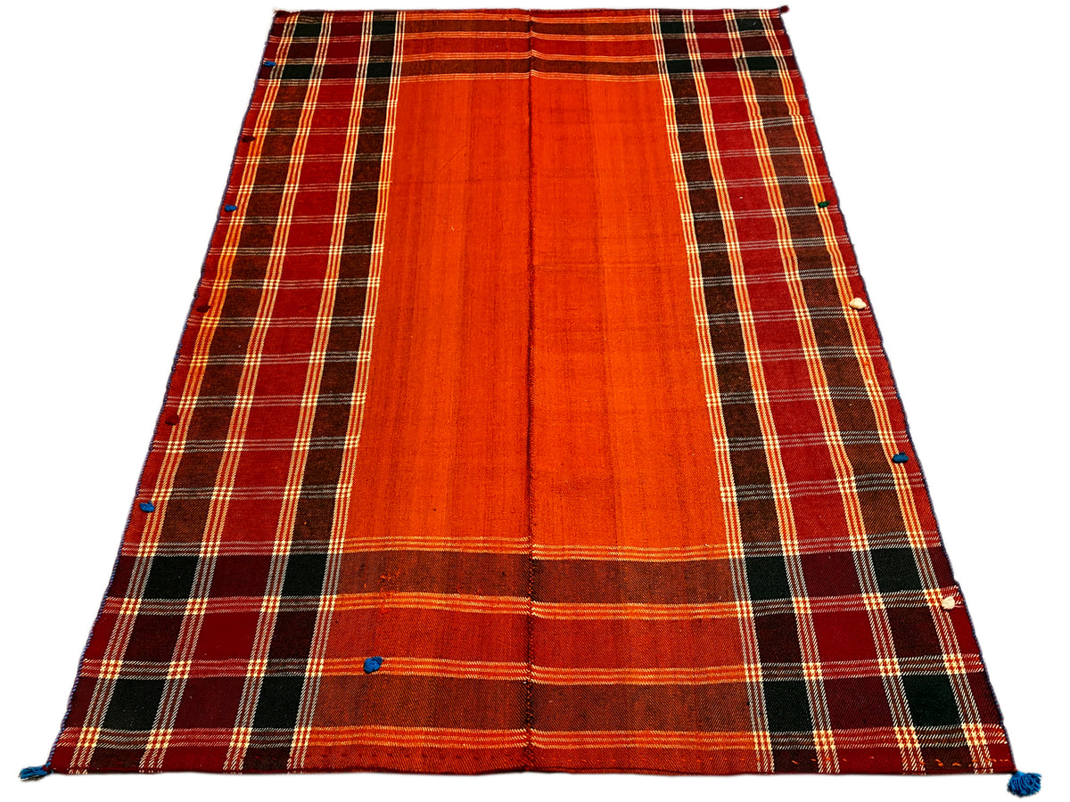 Jajim rug, lying at an angle: red-orange surface with a dark checkered border and blue fasteners