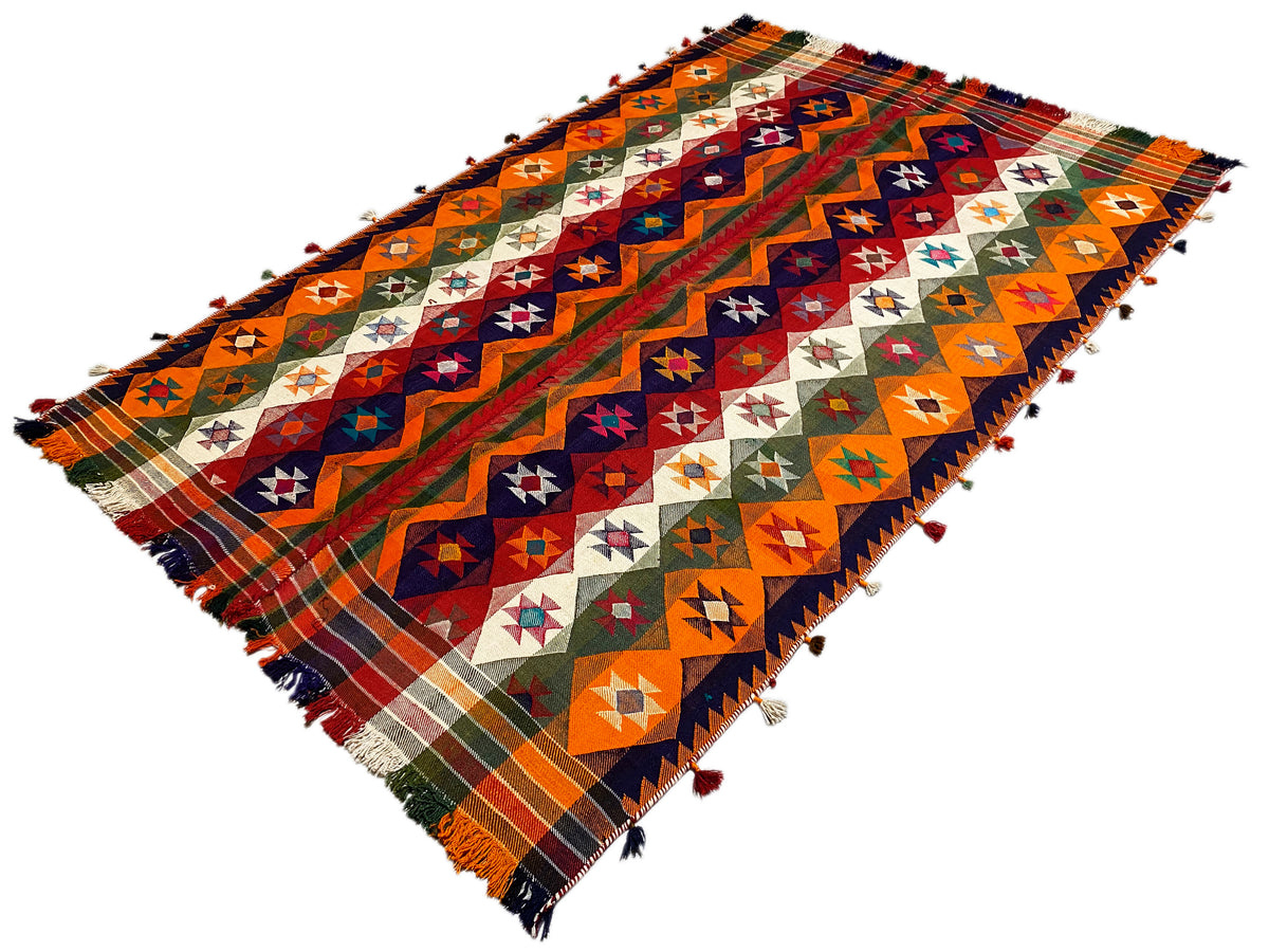 Jajim rug diagonal view: geometric shapes in orange, blue, and green, fringe