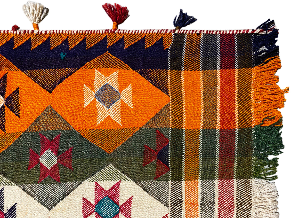 Close-up of a jajim rug: orange checkered and diamond patterns, fringes, and tassels