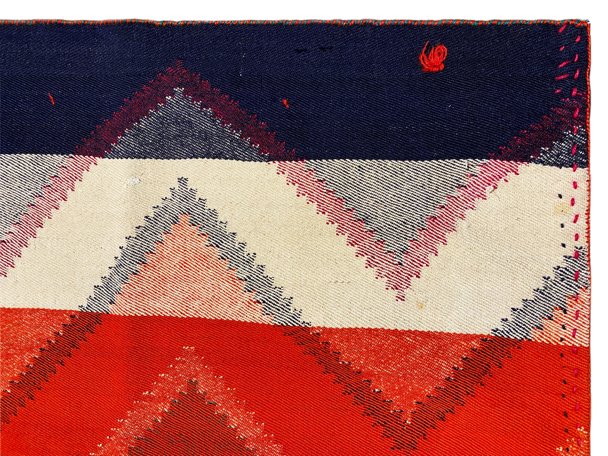 Rug edge with seam and geometric pattern in dark blue, cream, red, and gray