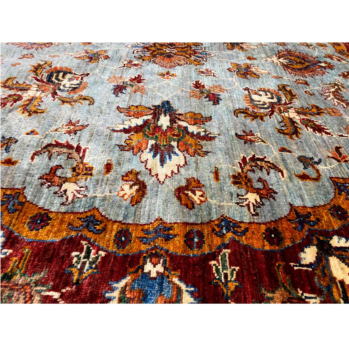 Close-up of the Kazak rug: light blue pile with colorful floral and ornamental motifs.