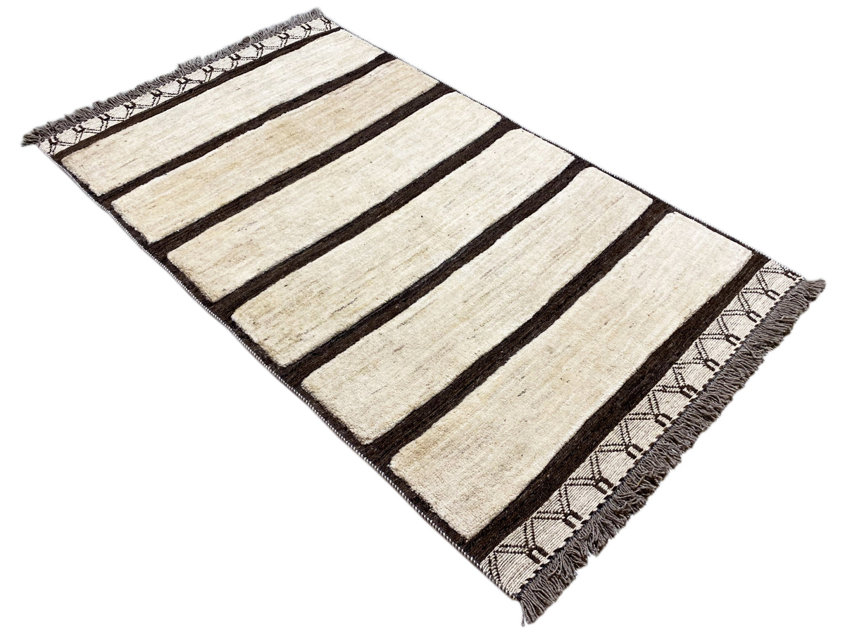 Kelim Gabbeh rug with cream-colored stripes and dark areas, angled view, fringes