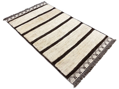 Kelim Gabbeh rug with cream-colored stripes and dark areas, angled view, fringes