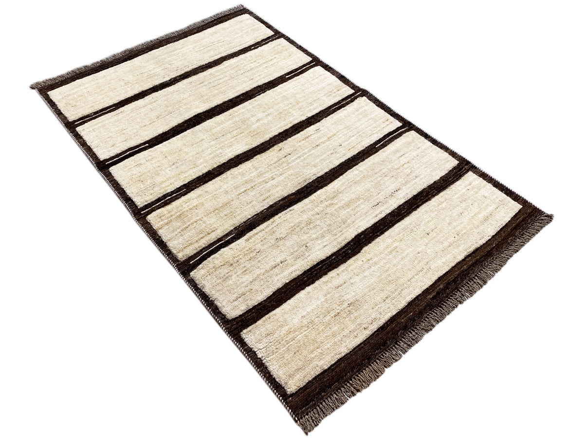 Rectangular beige kilim rug with dark stripes, photographed diagonally, with fringes.