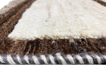 Close-up of the rug edge: soft beige pile, dark fibers underneath, with fringes.