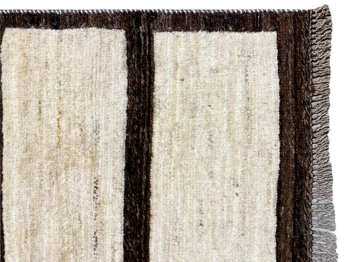 View of the top edge of the rug: beige striped pattern with a dark brown border and fringes.