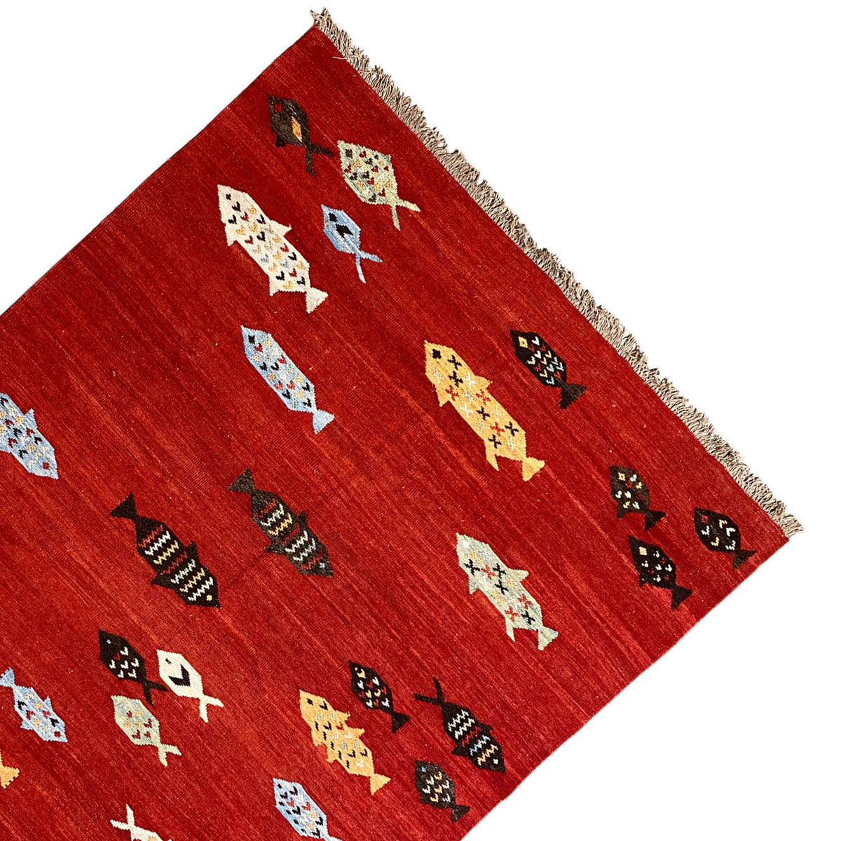 Corner of a red kilim rug with colorful motifs and fringes along the edge
