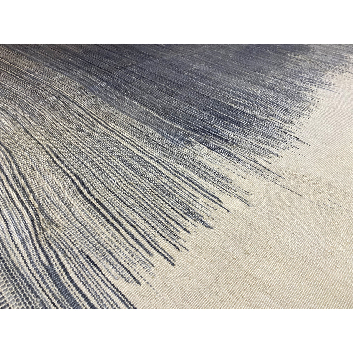 Close-up of a kilim rug: tightly woven lines, dark gray and cream, with fringes