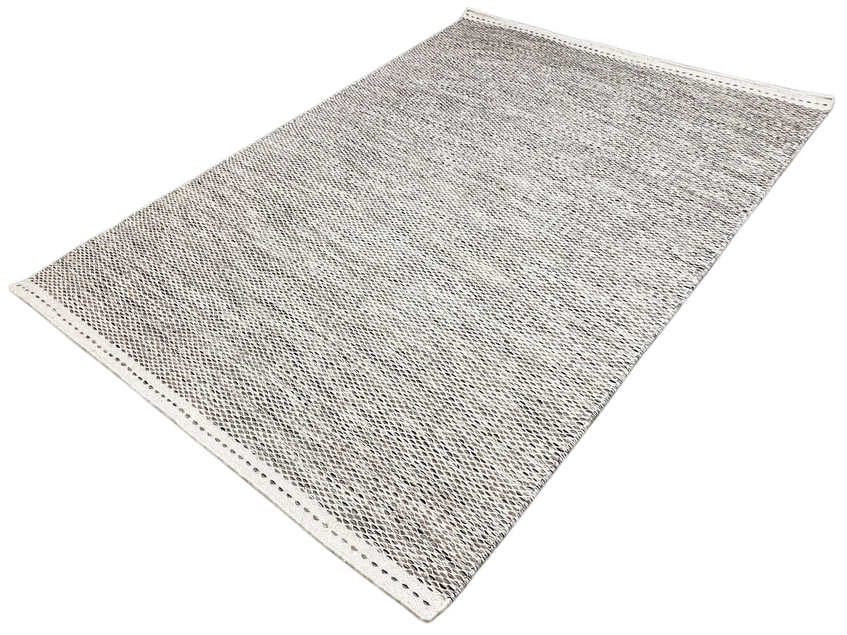 Light gray kilim rug with a dotted pattern, lying diagonally, visible bound edge