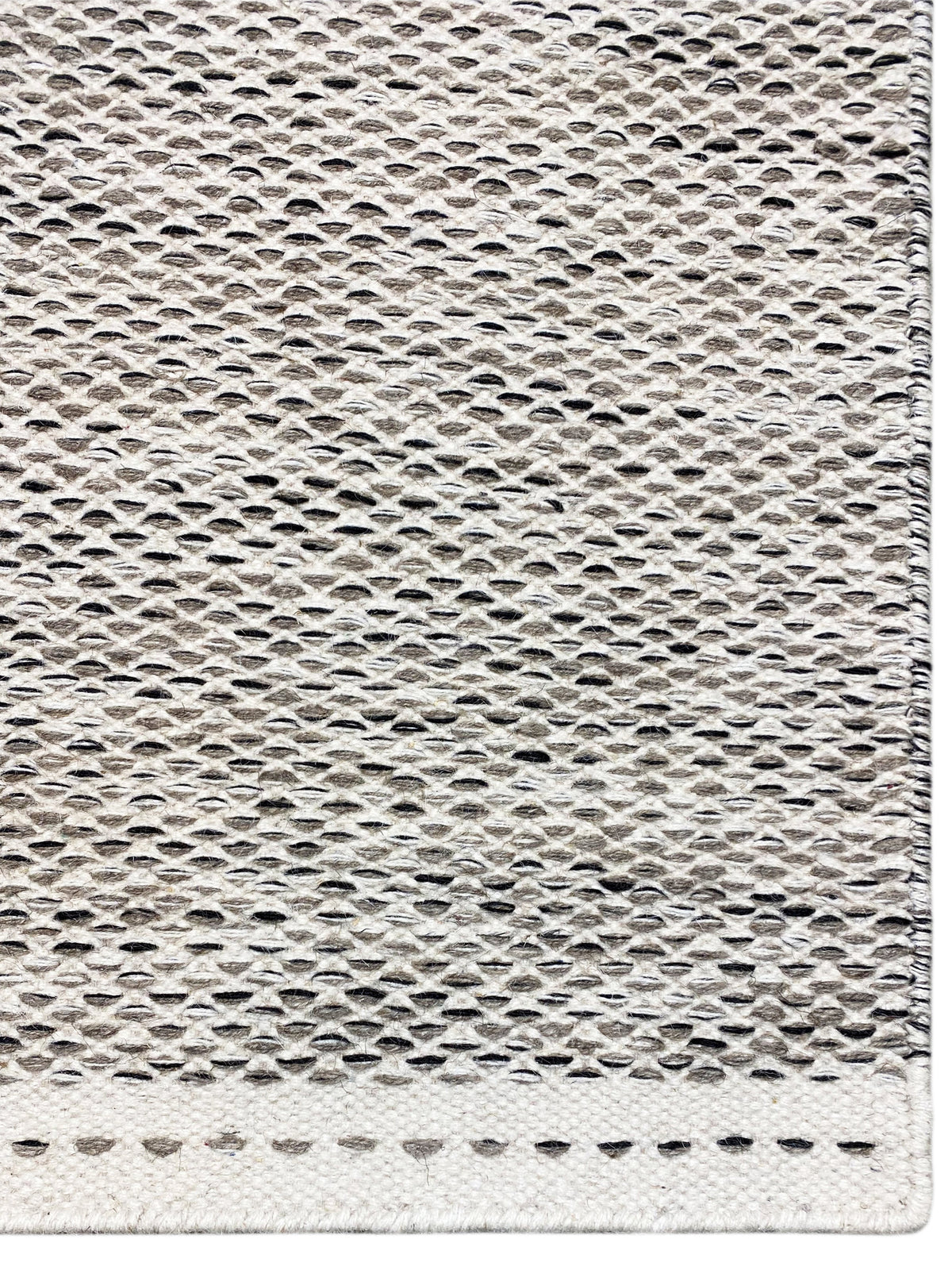Kilim rug edge view: woven texture in light gray with short fringe along the edge