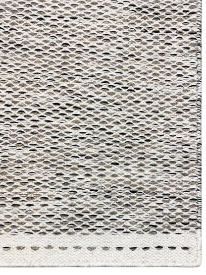 Kilim rug edge view: woven texture in light gray with short fringe along the edge