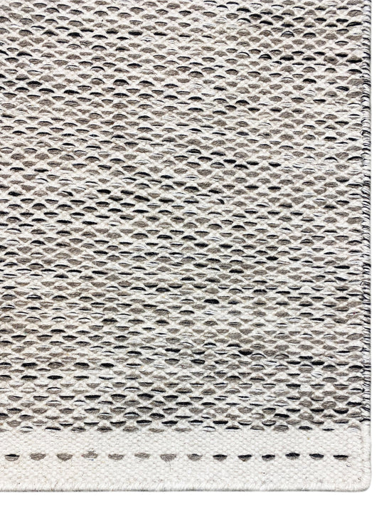 Kilim rug edge view: woven texture in light gray with short fringe along the edge