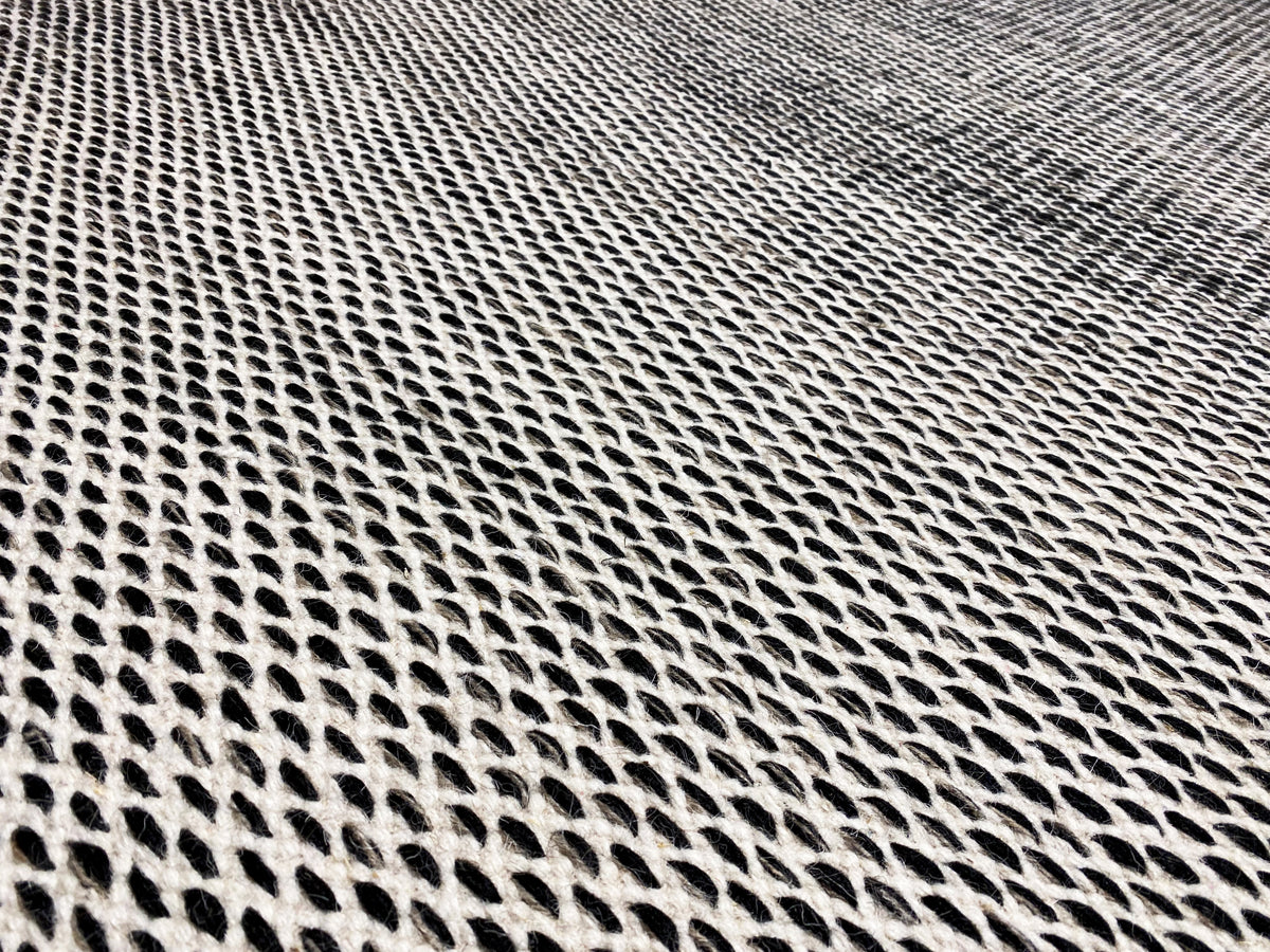 Kilim rug detail: dense dark gray grid weave, with a light-colored edge finish