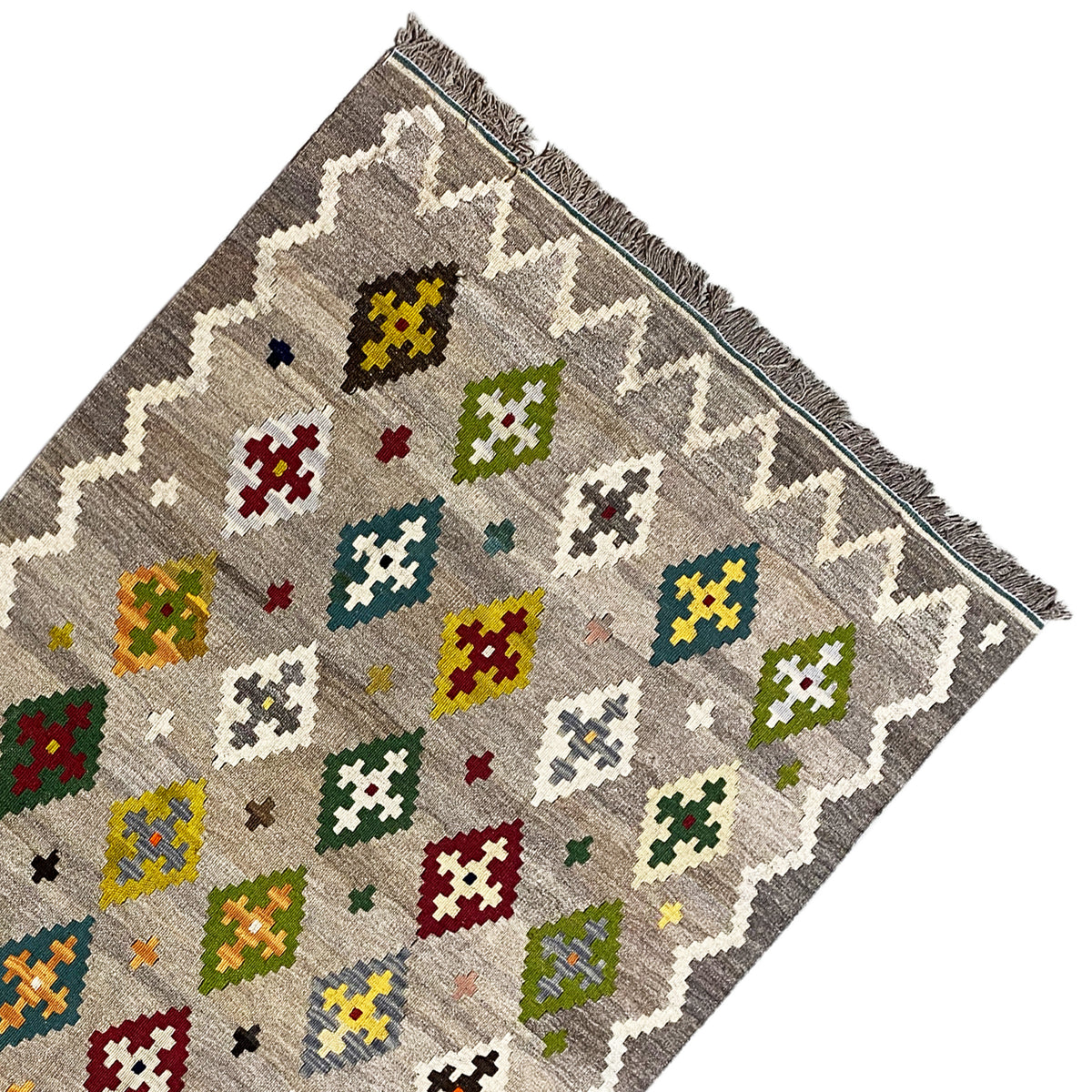 Kilim rug corner with colorful cross and diamond motifs on a gray background