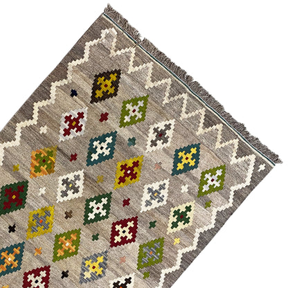 Kilim rug corner with colorful cross and diamond motifs on a gray background