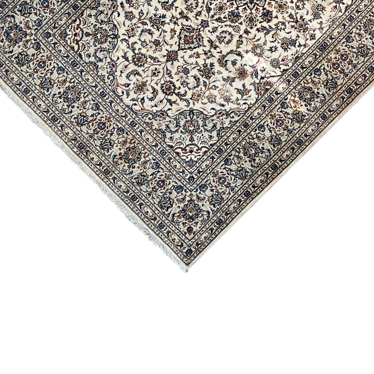 Keshan rug corner: beige ornamental field with a blue decorative border and fringes