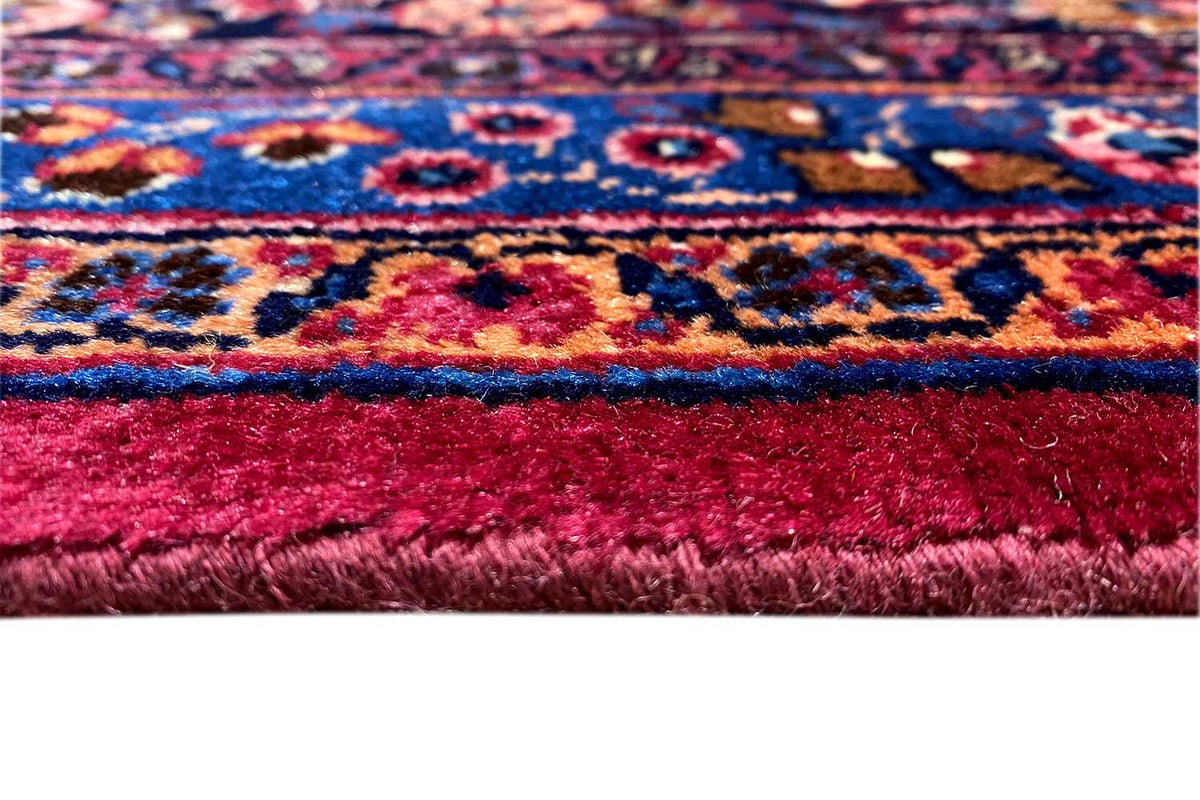 Oriental rug detail: red pile, blue patterned band, and fringe