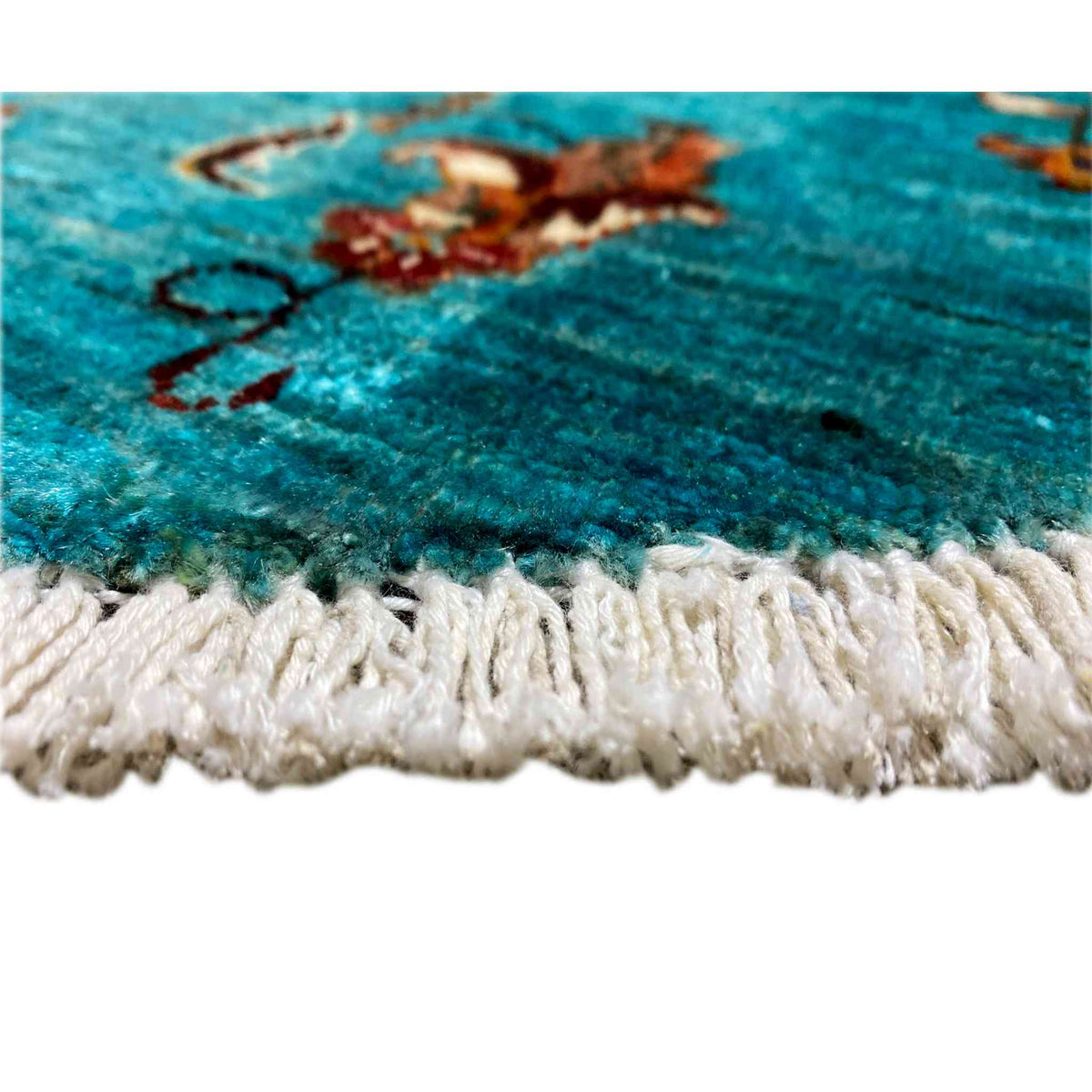 Close-up of the carpet edge: turquoise pile with a white-cream fringe trim.
