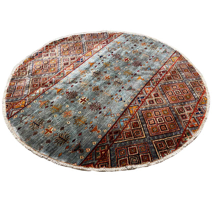 Round hand-knotted wool rug with a blue-gray background and colorful brown/orange ornaments