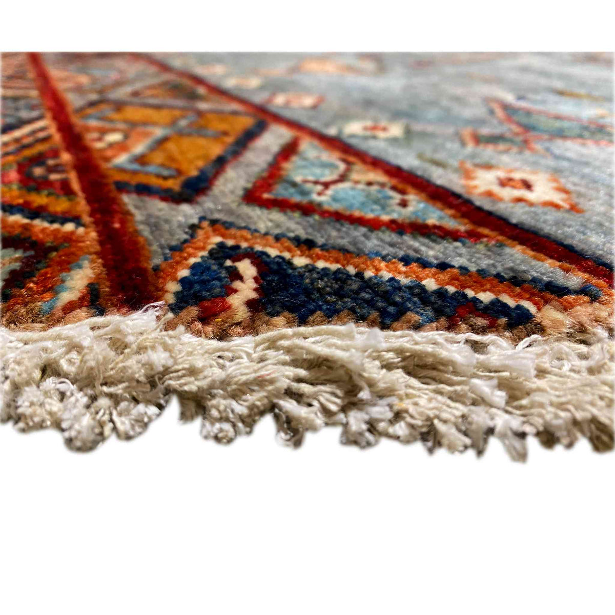 Close-up of the edge: hand-knotted wool rug with fringes in natural beige and colored lines