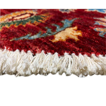 Carpet edge with white fringe trim along the edge of a wool rug with a red pattern
