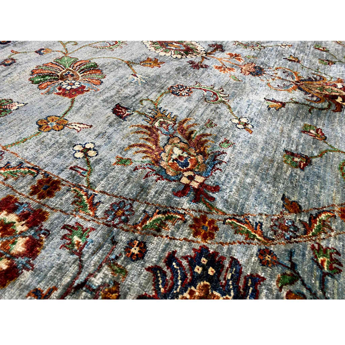 Close-up of a Khorjin wool rug: light blue-gray pile with colorful embroidered motifs