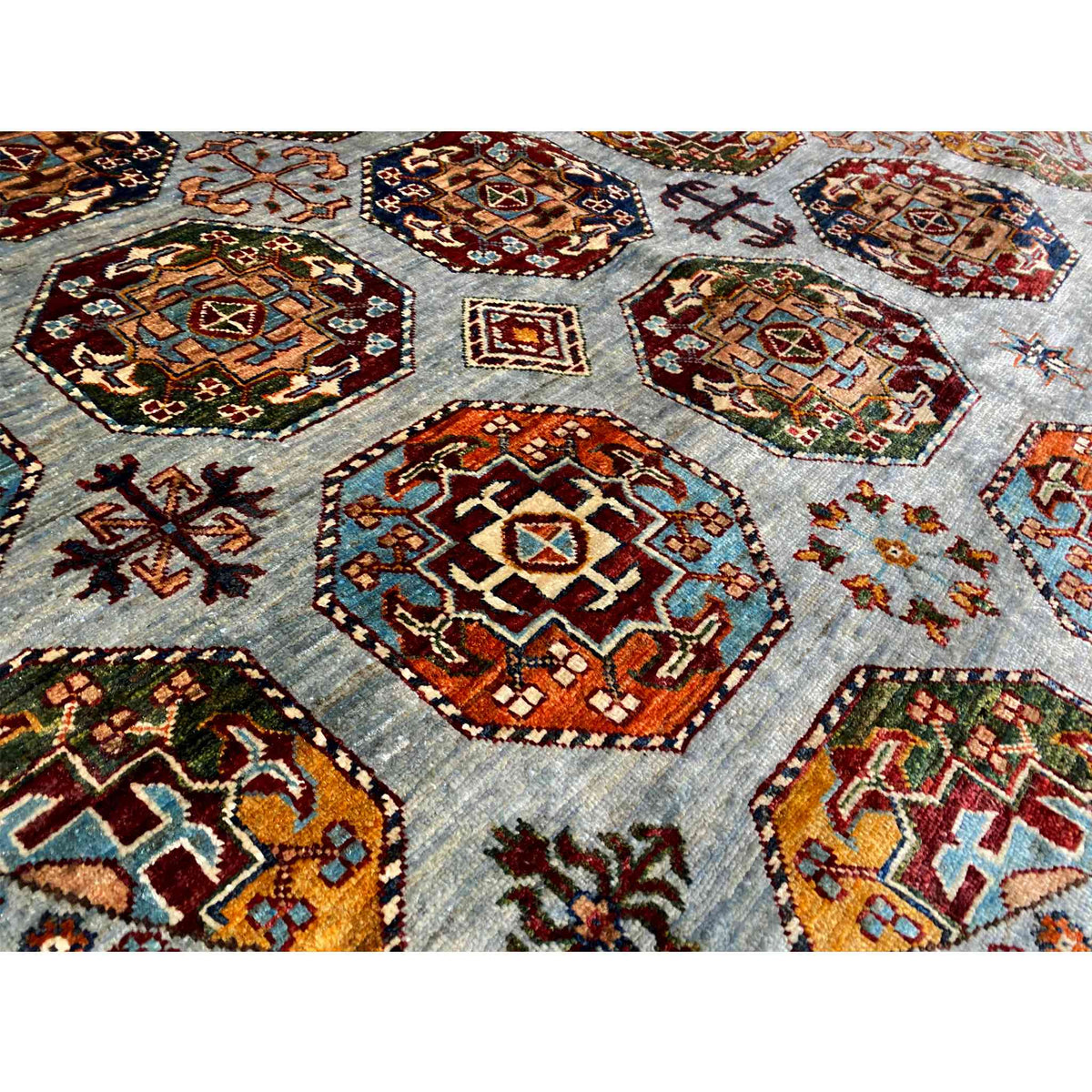 Rug detail with colorful hexagons, diamonds, and cross motifs on a blue-gray textile background