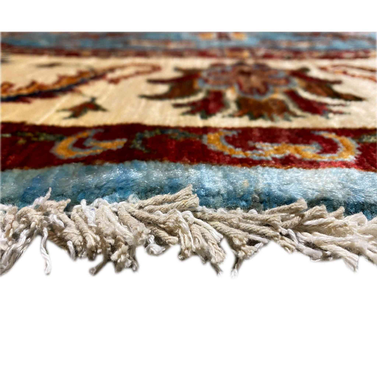 Carpet edge with white fringes and blue pile beneath ornamental stripes