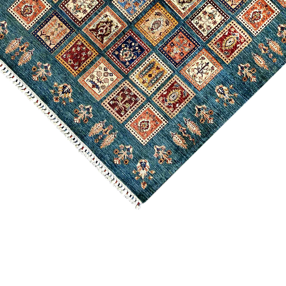 Teal rug with square patchwork, fringe at the corner, and multicolored ornaments