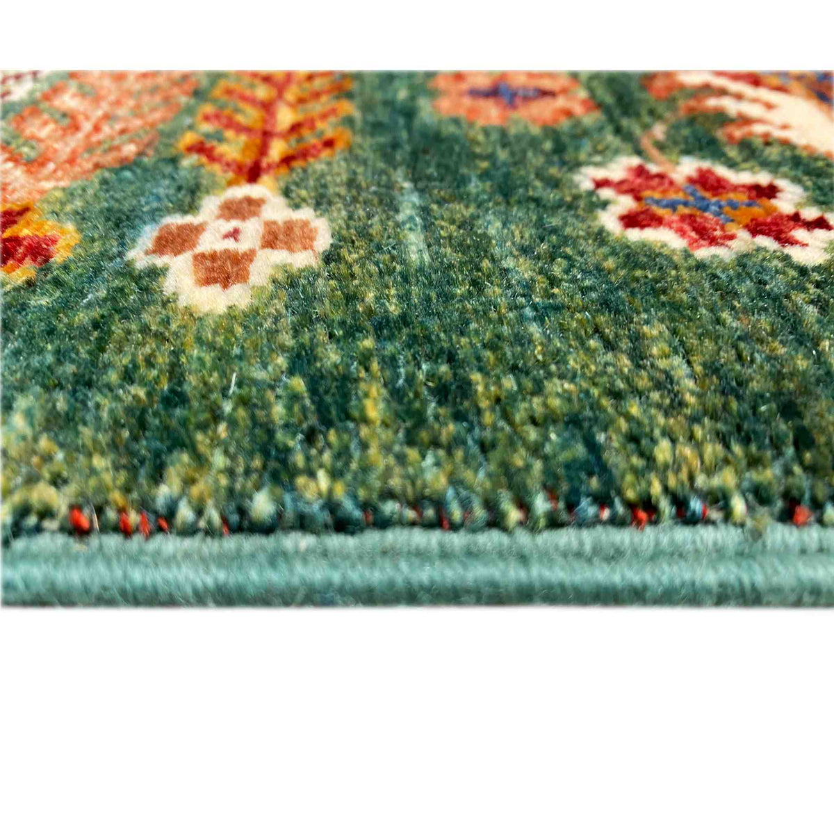 Close-up of a hand-knotted Khorjin rug: green pile with colorful patterned sections