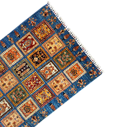 Corner view of the rug: blue pattern with tiled squares and white fringes
