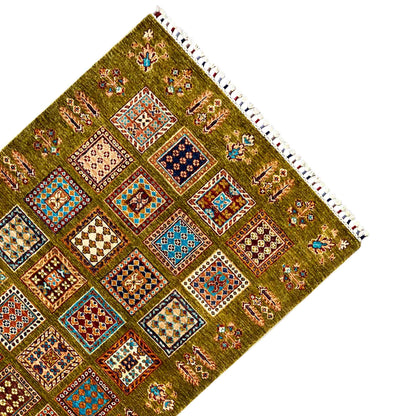 Corner of an olive-green wool rug with colorful patterns and white fringes