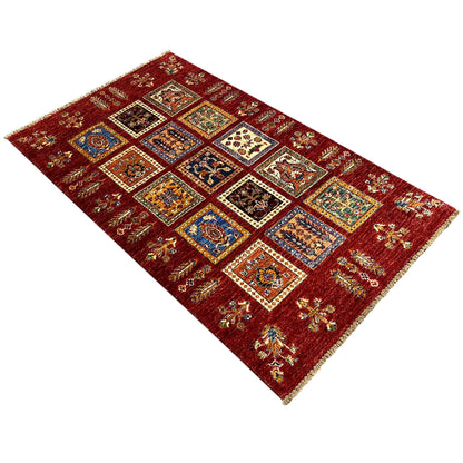 Deep red wool rug viewed diagonally with multicolored ornamental squares and decorative stripes