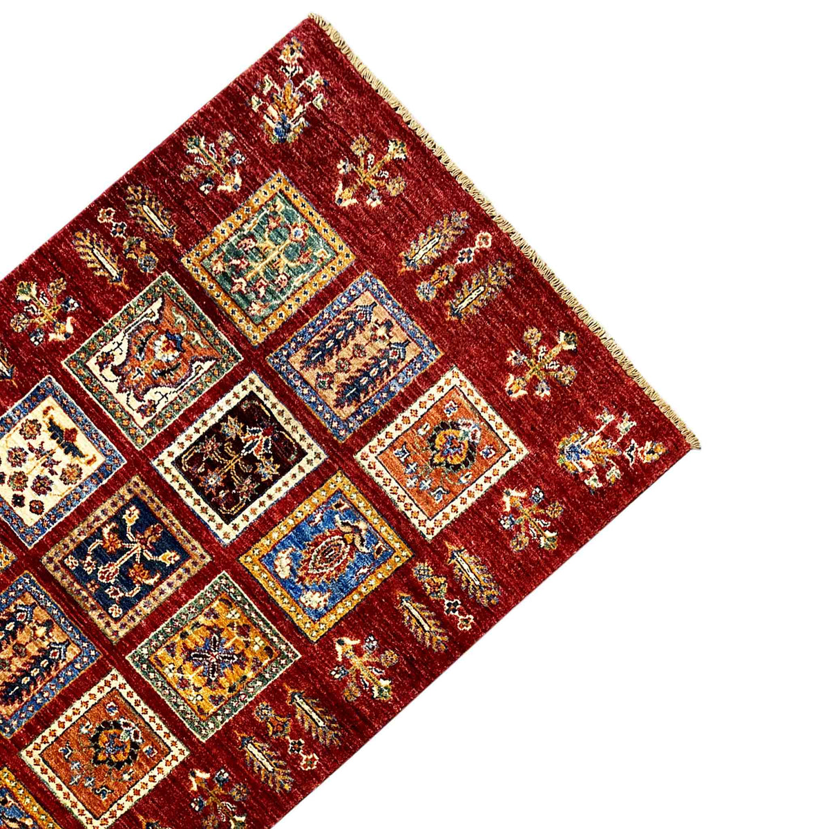 Deep-red wool carpet from the corner with decorative panels, colorful ornaments, and fringes along the edge