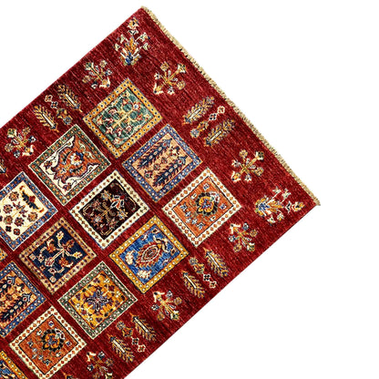 Deep-red wool carpet from the corner with decorative panels, colorful ornaments, and fringes along the edge
