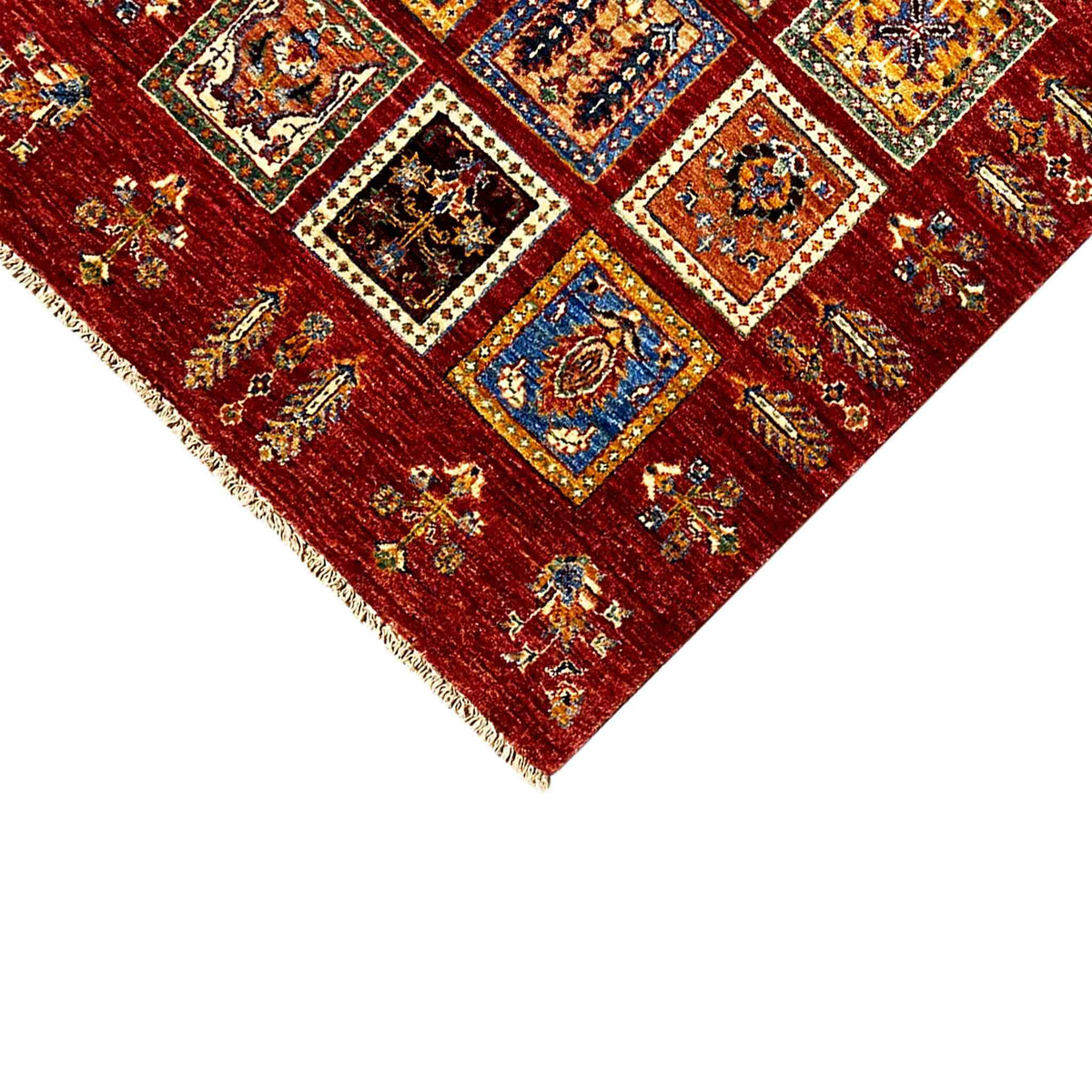 Close-up detail: deep-red wool rug with colorful squares and a visible fringed border