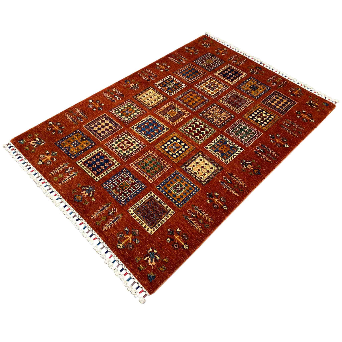 Brick-red wool rug with ornamental squares and white fringe along the edge, at an angle.