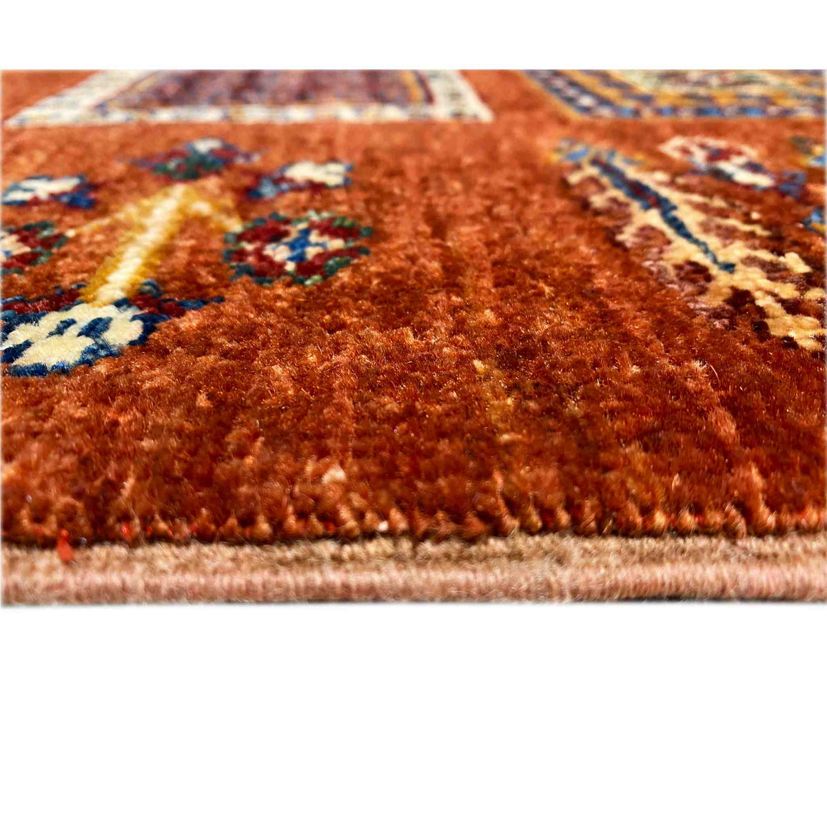 Brick-red wool rug in detail: dense pile and multicolored patterns along the edge.