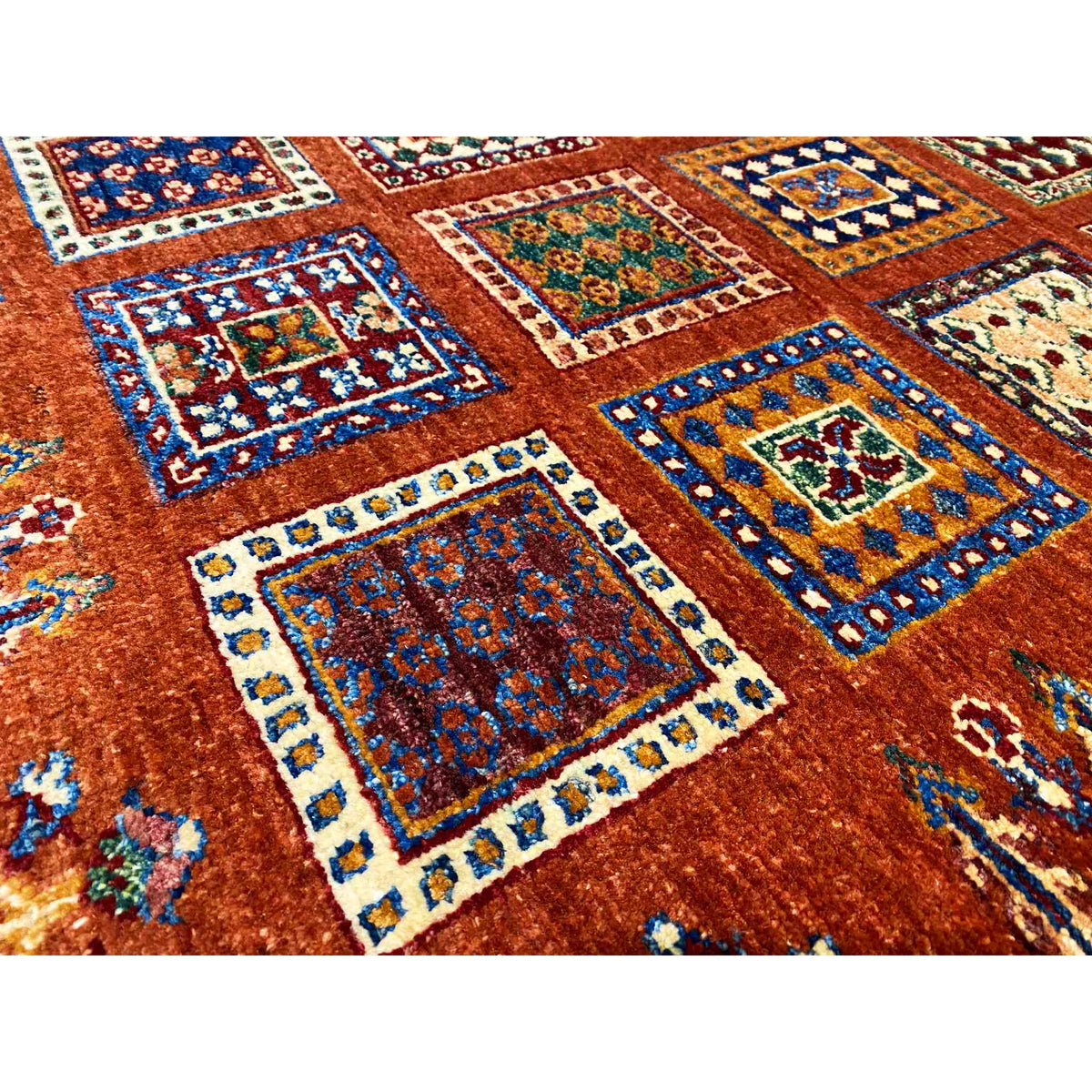 Wool rug in brick red with colorful squares and turquoise accents in the pattern, close-up.