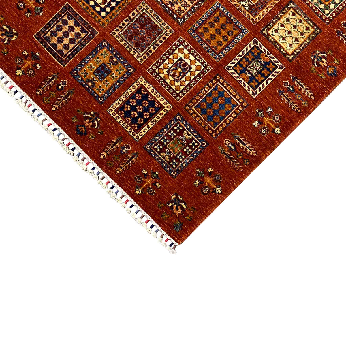 Corner area: brick-red wool rug with tile ornaments and white fringes, rectangular.