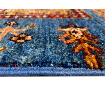 Close-up: blue carpet pile with colorful woven ornaments and fringe along the edge
