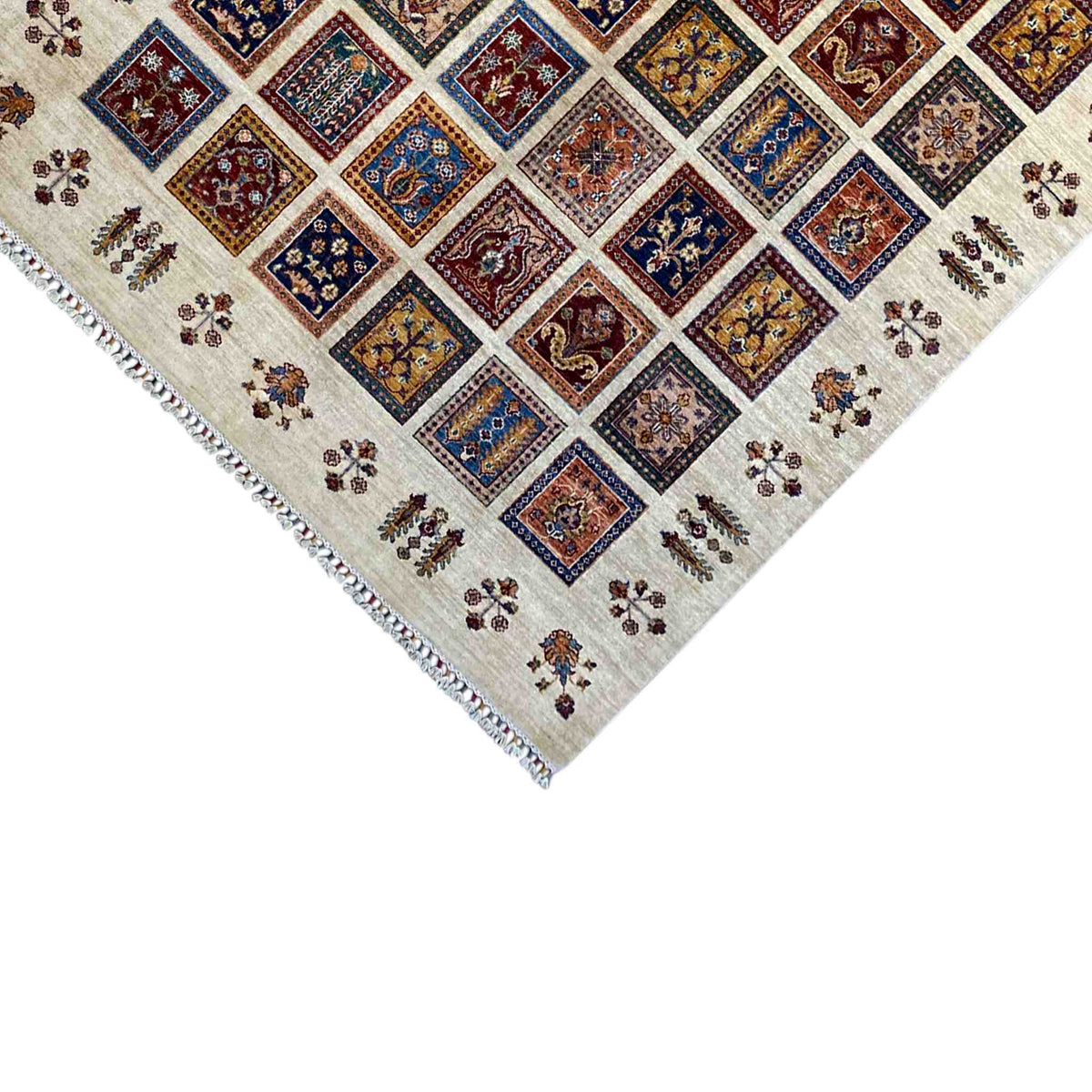 Corner of a beige rug with fringed edges and a colorful tile pattern